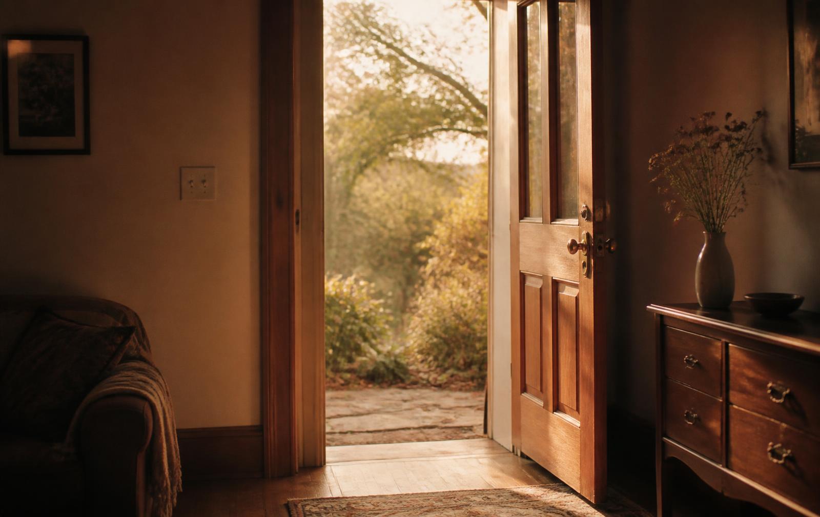 An open wooden door in a quiet room, with warm daylight and a garden beyond it